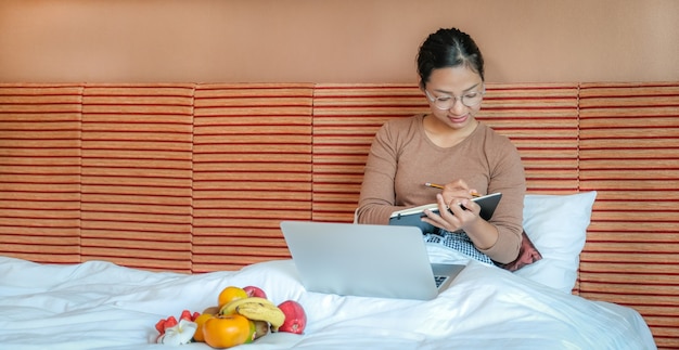 Los turistas usaban una computadora portátil y comían frutas en la cama en el concepto de comida saludable de la habitación del hotel de lujo