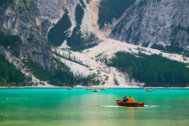 Los turistas viajan en barcos de madera en el lago Braies con aguas transparentes y dolomitas en el fondo en