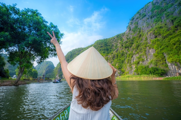 Foto turistas viajando en barcos a lo largo del río ngo dong en la parte de tam coc de la provincia de ninh binh, vietnam. los remeros usan sus pies para propulsar los remos. paisaje formado por torres cársticas y campos de arroz.