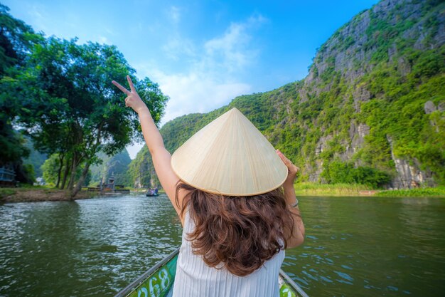 Turistas viajando em barcos ao longo do rio Ngo Dong na porção de Tam Coc, província de Ninh Binh, Vietnã, remadores usando seus pés para impulsionar remos. Paisagem formada por torres cársticas e campos de arroz