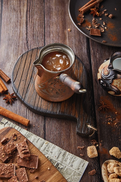 Turk com um cabo de madeira com cacau, chocolate com uma bebida quente em uma mesa de madeira, chocolate e canela, um café festivo. Lugar para texto