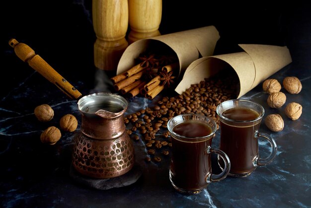 Turk y dos tazas de café caliente con especias, nueces y granos de café sobre un fondo oscuro Oscuro y malhumorado