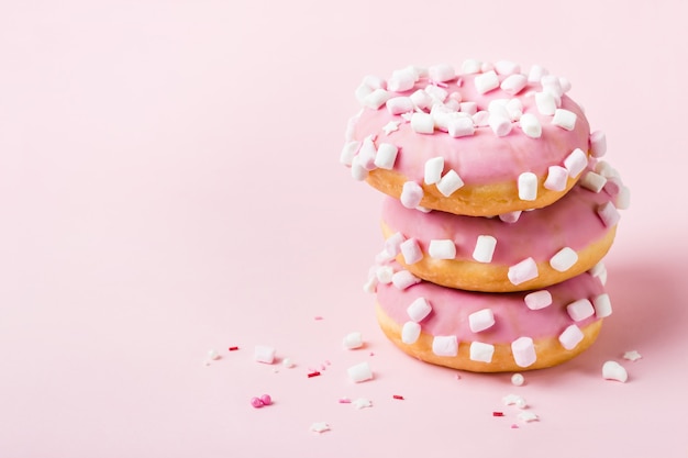 Turm aus rosa glasierten Donuts mit Marshmallows auf rosa Hintergrund.