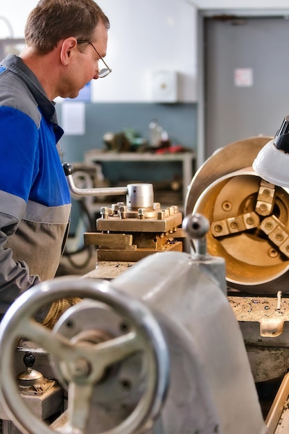 Foto turner anciano de 5055 años en overoles trabaja en torno en taller de producción procesamiento de productos metálicos