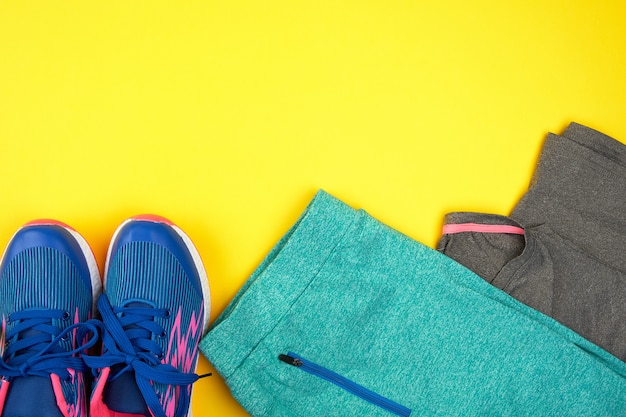 Turnschuhe und Kleidung der blauen Frauen für Sport auf einem gelben Hintergrund