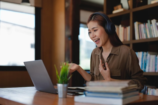 Tutor asiático de idioma comienza la lección en línea con la mano de la onda del aprendiz sonriendo mira a la mujer de la pantalla de la PC en los auriculares que se comunican a distancia el concepto de uso de la aplicación del proceso de aprendizaje electrónico