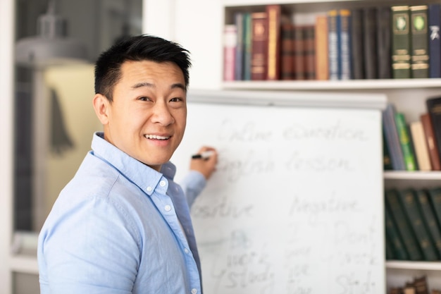 Tutor coreano hombre escrito en pizarra enseñando inglés en el aula