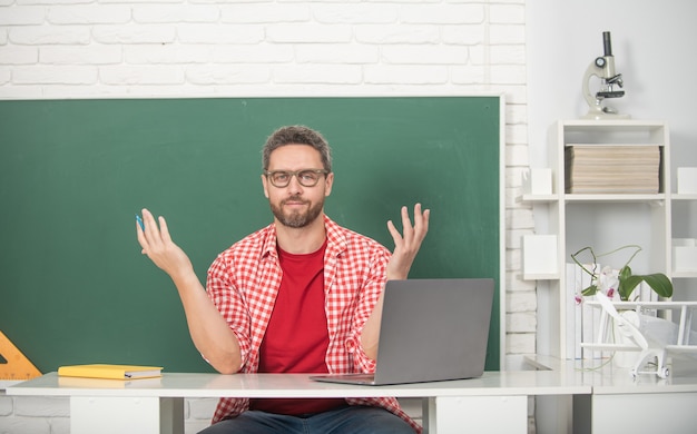 Tutor de homem adulto sorridente sentado em sala de aula no quadro-negro, educação.