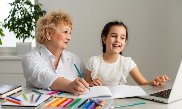 Tutor de mulher ou mãe adotiva ajudando uma menina de escola caucasiana bonita fazendo lição de casa sentada à mesa. Diversas babá e criança aprendendo a escrever no caderno estudando em casa.