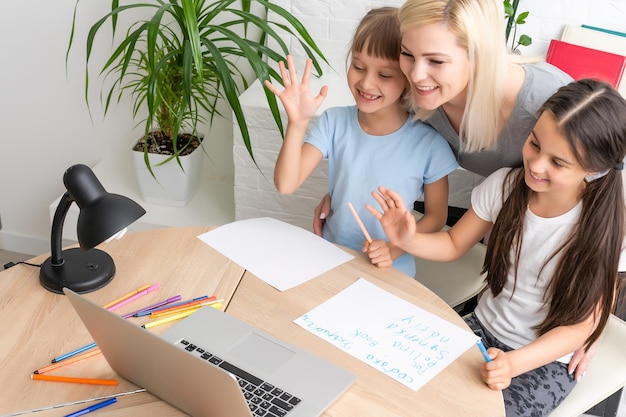 Tutor de mulher ou mãe adotiva ajudando uma menina de escola caucasiana bonita fazendo lição de casa sentada à mesa. Diversas babá e criança aprendendo a escrever no caderno estudando em casa.