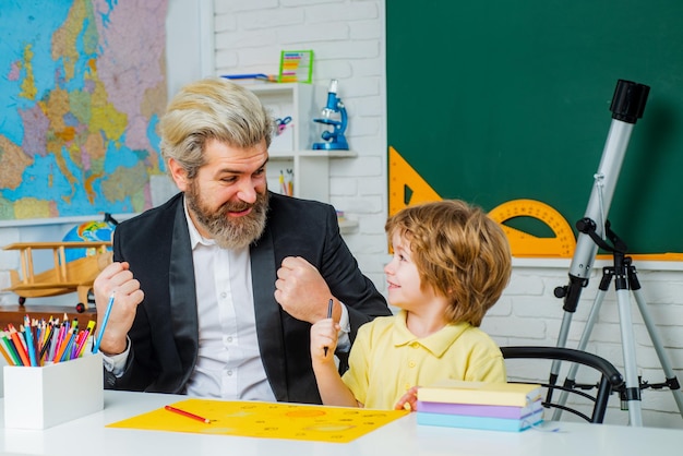 Tutor de escuela primaria educación preescolar niño lindo niño con maestro en el aula cerca de la pizarra