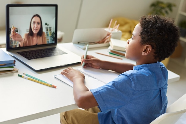 Tutor feminino explicando a solução da tarefa para o menino negro enquanto trabalhava com ele via aplicativo de videoconferência