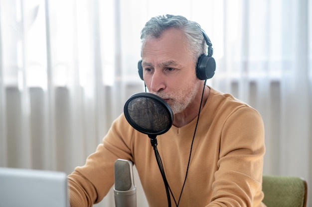 Foto tutorial en línea. un hombre de pelo gris con auriculares negros hablando en el micrófono y mirando ocupado