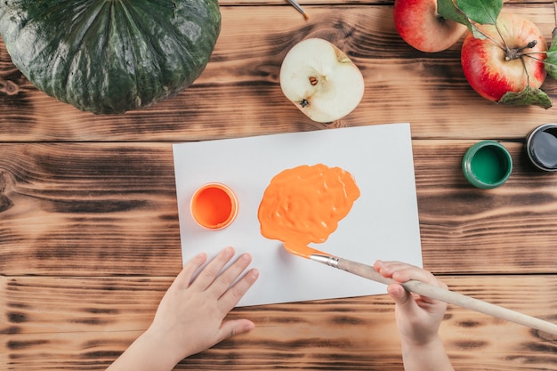 Tutorial paso a paso de Halloween con estampados de calabaza y manzana. Paso 5: Las manos de los niños pintan el papel con pintura naranja. Vista superior