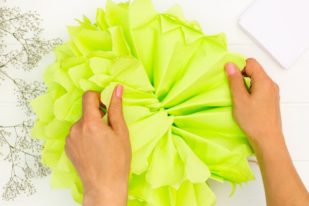 Tutorial passo a passo sobre como fazer um pompom fofo verde claro de papel de seda em uma mesa de madeira branca