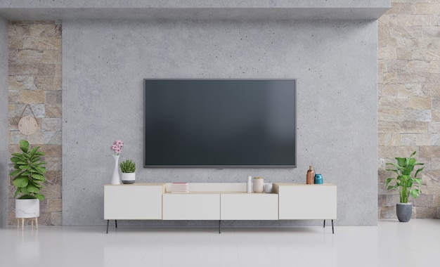 TV en el gabinete en la moderna sala de estar con lámpara, mesa, flor y planta en la pared de cemento.