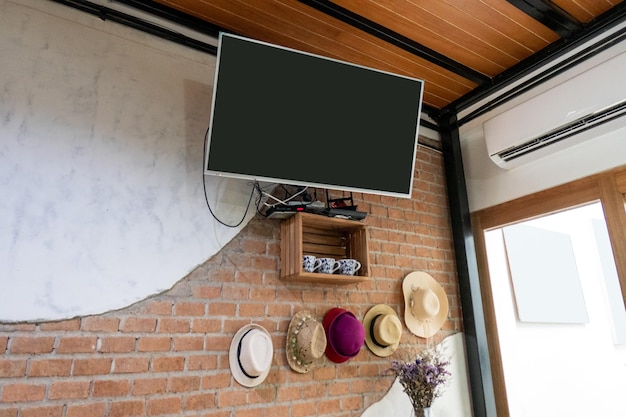 Foto tv plana colgada en la pared de ladrillo con sombrero y decoración de flores