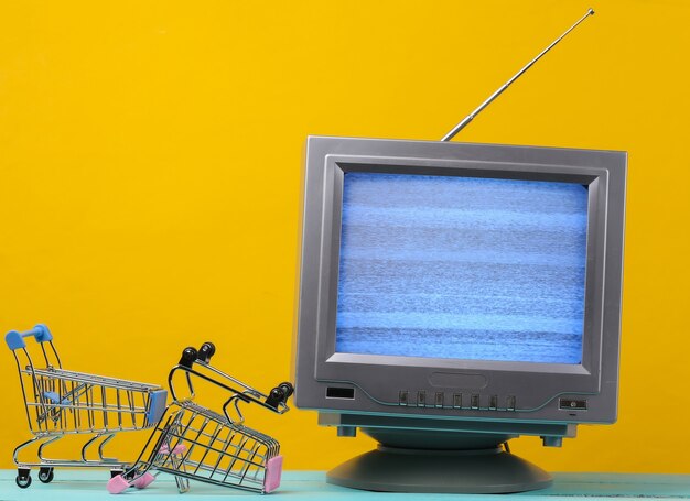 TV-Shop. Antenne altmodischer Retro-Fernseher mit Mini-Supermarktwagen auf Gelb