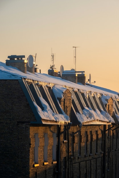 Foto tv- und kabelantennen auf dem dach eines mehrfamilienhauses bei sonnenuntergang mit schnee bedeckt.