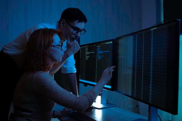 Two software developers collaborating at night focusing on code review and debugging process on a computer screen representing teamwork innovation and modern software development workflow