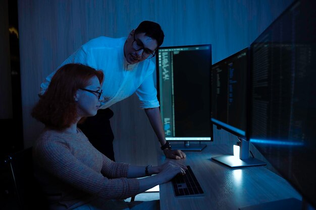 Two software developers collaborating at night focusing on code review and debugging process on a computer screen representing teamwork innovation and modern software development workflow