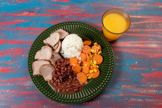 Typisch brasilianisches Gericht mit Reis, roten Bohnen, Schweinefleisch und Karottensalat und geschmortem Mais in einem grünen Teller