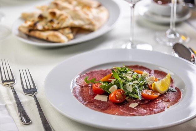 Foto typisch italienisches vorspeisen-carpaccio vom kalb oder rind, in dünne scheiben geschnitten und auf einem teller mit salat serviert