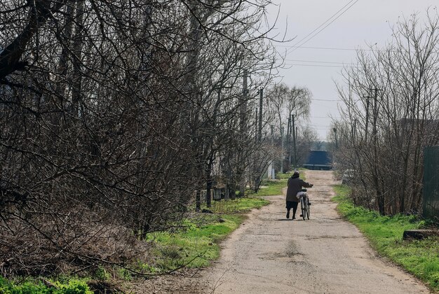 Typische Dorfstraße in der Ukraine, Frau trägt Fahrrad