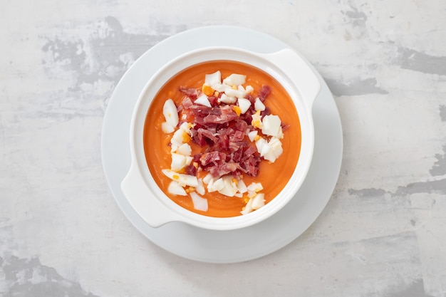 Typische Salmorejo-Creme der spanischen Suppe mit Schinken und Ei in der weißen Schüssel auf keramischem Hintergrund