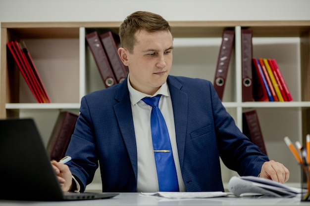 Typischer Arbeitstag. Nahaufnahme eines selbstbewussten jungen Geschäftsmannes, der in seinem Büro sitzt und den Laptopbildschirm betrachtet.