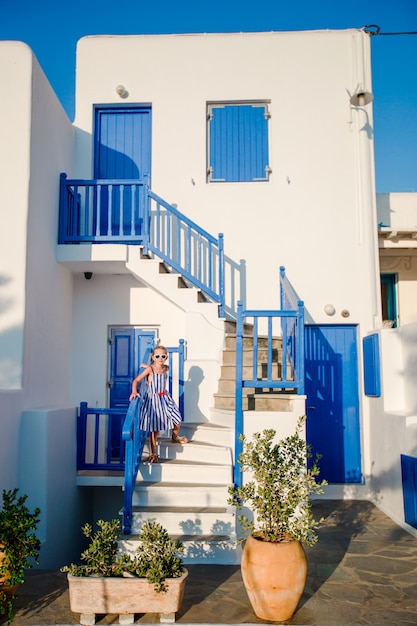 Typisches Haus mit blauen Balkonen, Treppen und Blumen. Kleines Mädchen auf Treppen im traditionellen griechischen Haus. Schönes Architekturgebäude außen mit kykladischem Stil.