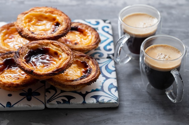 Typisches portugiesisches Eierkuchenpastell de Nata mit Tasse Kaffee auf Keramikhintergrund