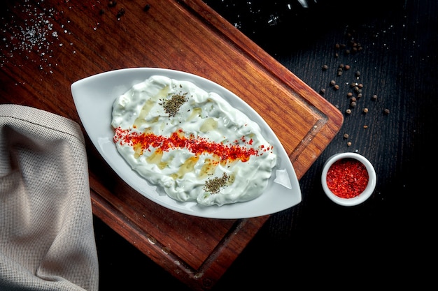 Foto tzatziki, cacä ± k oder tarator ist eine traditionelle türkische und griechische vorspeise aus frischem joghurt, gurken, gewürzen und olivenöl auf einem weißen teller. dunkel