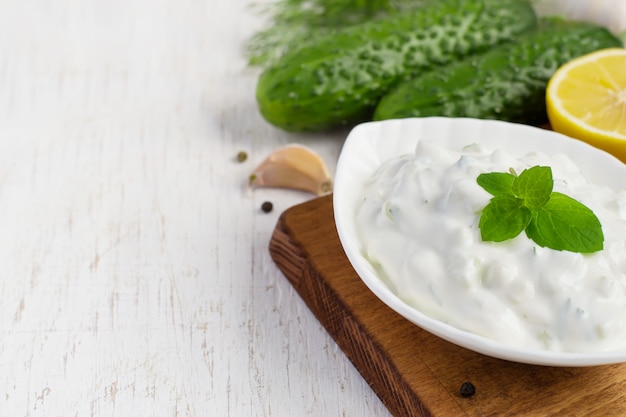 Tzatziki-Sauce in einer Schüssel und Zutaten - Gurke, Minze, Dill, Zitrone, Knoblauch