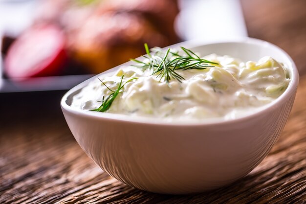 Tzatziki. Tzatziki-Sauce-Dip oder Dressing mit Hähnchengrillbeinen im Hintergrund.