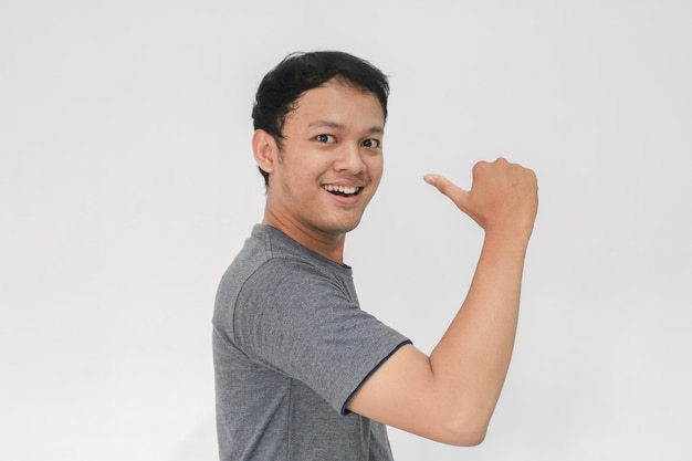 Uau e rosto surpreso com sorriso de jovem asiático em camiseta cinza com ponto de mão no espaço vazio