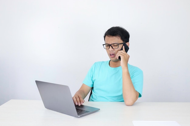 Uau, o rosto de um jovem asiático chocou o que vê no laptop ao ligar para o telefone indonésio vestindo camisa azul