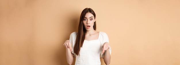 Uau, olhe lá, jovem maravilhada de vestido branco, apontando os dedos para baixo, admirada com a queda