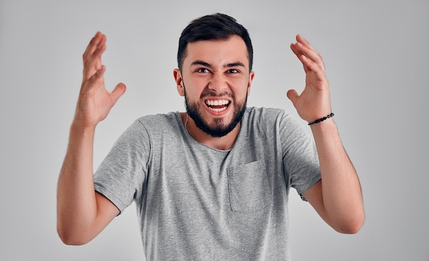 Uau. Retrato frontal com metade do comprimento masculino atraente em estúdio cinza backgroud. Jovem emocional surpreso barbudo em pé com a boca aberta. Emoções humanas, conceito de expressão facial