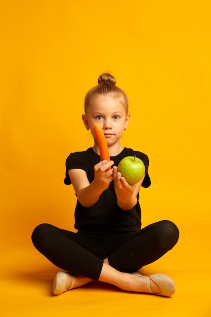 Uau, seu fundo amarelo menina surpresa orgânica criança pequena segurando maçã orgânica e cenoura comendo comida orgânica natural decisão orgânica saúde escolar