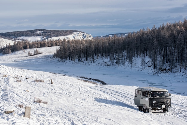 UAZ - russischer Van im Grasland mit schneebedeckten Bergen auf Hintergrund in Mongolei