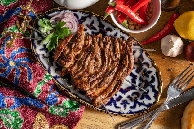 Uch - panja de cordero. Cordero y costillas de cordero marinadas con especias y fritas a la parrilla en tres brochetas en un plato uzbeko con cebollas rojas y hierbas frescas.