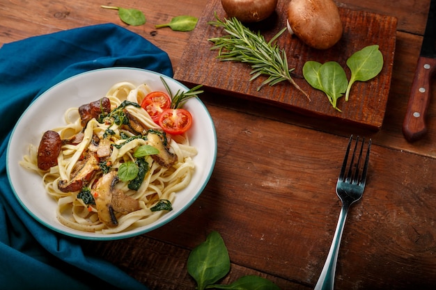 Udon com cogumelos e espinafre em um prato em um guardanapo azul ao lado de um garfo e cogumelos