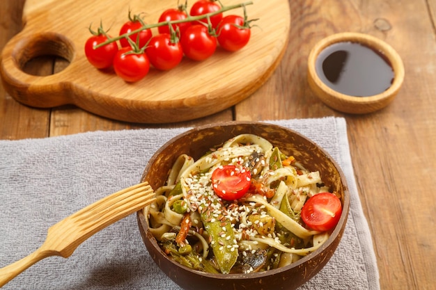 Udon com legumes e cogumelos na mesa em uma placa de madeira ao lado de champignon e tomate em uma prancha