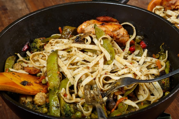 Udon com legumes e frango com sementes de gergelim e cogumelos em uma frigideira