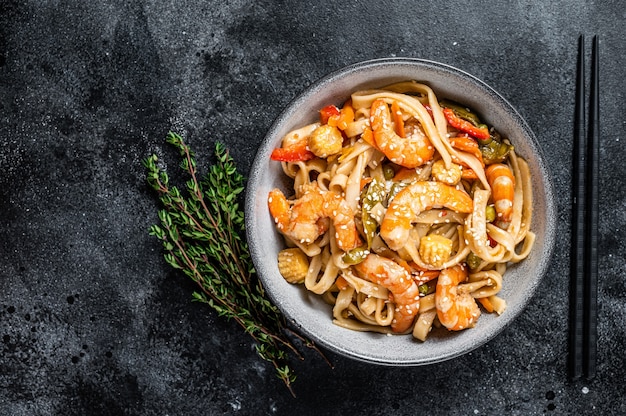 Udon-Meeresfrüchte-Nudeln mit Garnelen in einer Schüssel anbraten. Schwarzer Hintergrund. Ansicht von oben. Platz kopieren.