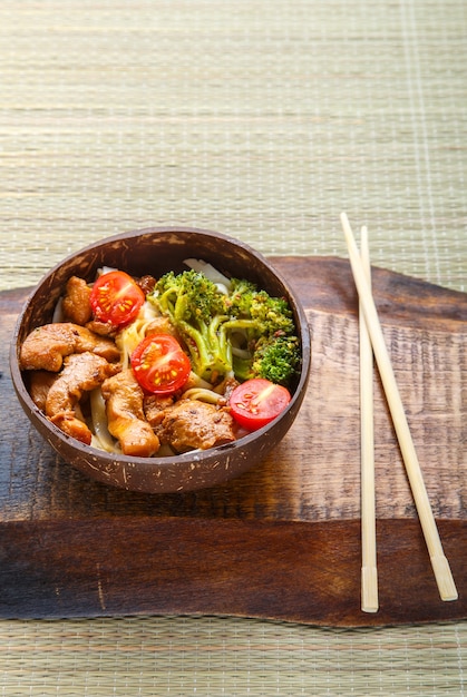 Udon mit Fleisch in japanischer Soße auf einem Teller mit Kokoschips auf einem Stäbchenständer. Vertikales Foto