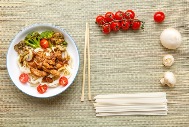 Udon mit Fleisch in japanischer Soße auf einem Teller neben Gemüse und Stäbchen Horizontales Foto