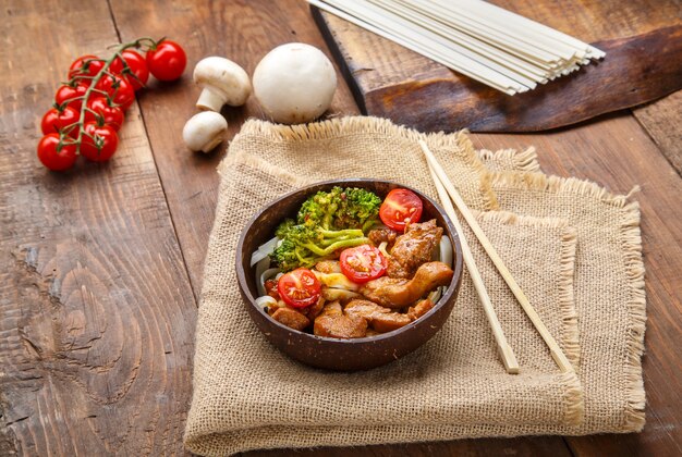 Udon mit Hühnchen in japanischer Sauce auf einem Teller mit Kokosnussschalen auf einer Serviette neben Stäbchen. Horizontales Foto