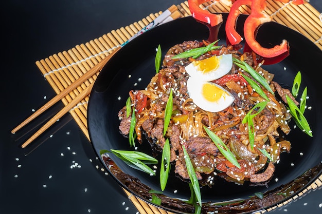 Udon-Nudeln mit Fleisch, Pilzen und Gemüse, bestreut mit Sesamsamen Asiatischer Braten auf schwarzem Hintergrund